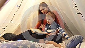 Little boy playing in children`s tent at home. Mother reading fairy tale book. Happy caucasian kid in the playroom.