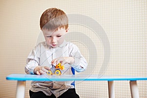 Little boy playing with colored toy car on a table