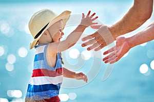 Little boy playing with father at the beach in straw hat