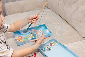 a little boy playing fisherman catches wooden fish in a box with a toy fishing rod with a magnet.