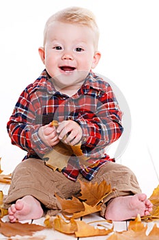 Little boy playing on the floor with maple leaves.