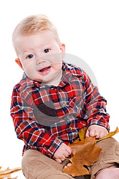 Little boy playing on the floor with maple leaves.