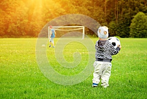 Little boy playing football on the field with gates