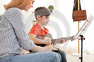 Little boy playing guitar with his teacher at music lesson