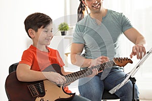 Little boy playing guitar with his teacher at music lesson