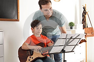 Little boy playing guitar with his teacher at music lesson