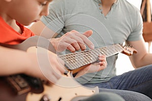 Little boy playing guitar with his teacher at music lesson. Learning notes