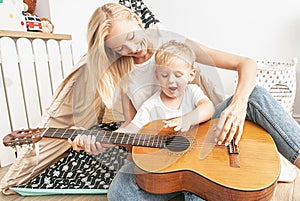 Little boy playing on guitar with mom