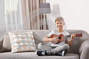 Little boy playing guitar on sofa in room