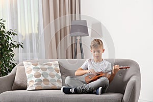 Little boy playing guitar on sofa in room