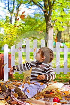 Little boy playing with leaves and eating cookies in the autumn