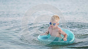 Little boy playing in ocean sea water, child having fun, swimming on blue swimming ring. Summer vacation, holiday