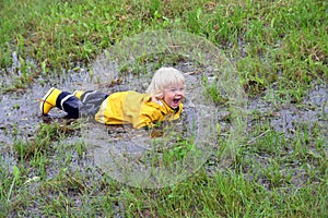Little boy playing outdoor in a muddy puddle on a rainy fall day