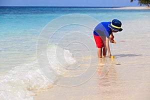 Little boy playing with paper boat at beach