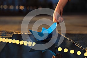 Little boy playing with paper boat near puddle outdoors, closeup