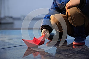 Little boy playing with paper boat near puddle on pier, closeup