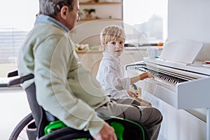 Little boy playing on the piano with his grandfather on wheelchair.