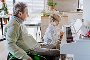 Little boy playing on the piano with his grandfather on wheelchair.