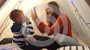 Little boy playing playing with his mother in children's tent at home. Happy caucasian kid in the playroom.