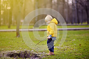 Little boy playing with puddle and stick during stroll in the park