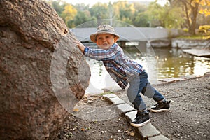 A little boy is playing and pushing a rock during a walk in the