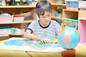 Little boy playing with puzzle of map in class