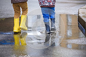 Little boy playing in rainy summer park. Child with colorful rainbow umbrella, waterproof coat and boots jumping in puddle and mud