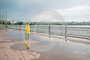 Little boy playing in rainy summer park. Child with umbrella, waterproof coat and boots jumping in puddle and mud in the