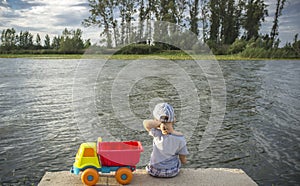 Little boy playing at riverside with dump truck loaded with stones