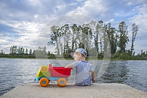 Little boy playing at riverside with dump truck loaded with stones