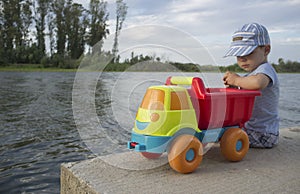 Little boy playing at riverside with dump truck loaded with stones