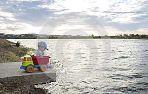 Little boy playing at riverside with dump truck loaded with stones