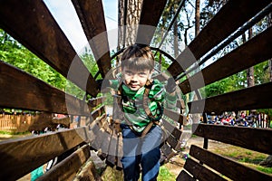 Little boy playing at rope adventure park. Summer holidays concept. Cute child having fun in net tunnel. Modern amusement park for