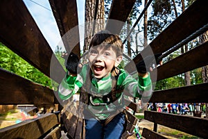 Little boy playing at rope adventure park. Summer holidays concept. Cute child having fun in net tunnel. Modern amusement park for