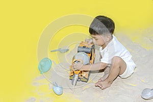 Little boy  playing sand  with cement truck toy on yellow background .