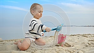 Little boy playing on the sandy beach with toys and using a shovel to dig sand. Happiness and excitement of a family vacation and