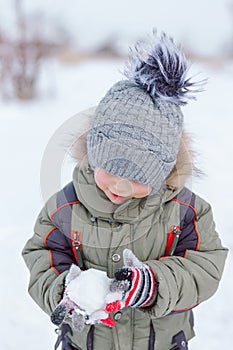 Little boy playing with snow, holding a lump of snow in his hands