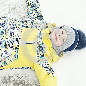 Little boy playing in the snow, portrait, lying on his back, laughing