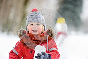 Little boy playing with snowballs with snowman on background