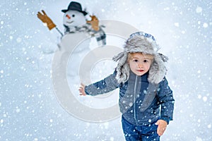 Little boy playing with snowman in winter park. Winter portrait of cute child in snow Garden. People in snow. Happy