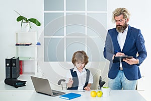 Little boy playing to be boss on a business desk in office. Businessmans crew working with new startup project in office