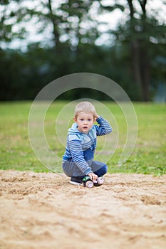 Little boy playing with a toy car in the sandbox on children playground