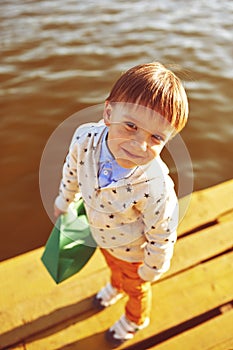 Little boy playing with toy paper ship by the lake