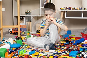 Little boy playing with toys sitting on the floor among scattered toys, a mess in the children's room