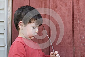 little boy playing with twigs in the backyard by the garage