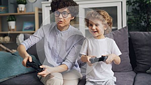 Little boy playing video games with excited mom holding joysticks at home