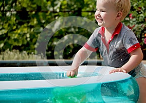 A little boy is playing with water near an inflatable pool. Summer and family holidays. Happy childhood
