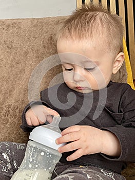 A little boy plays with a baby bottle with a nipple filled with milk formula for feeding