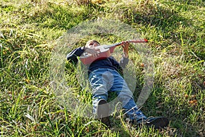 A little boy plays the guitar while lying on the green grass in the park