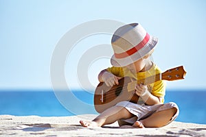 Little boy plays guitar ukulele at sea beach